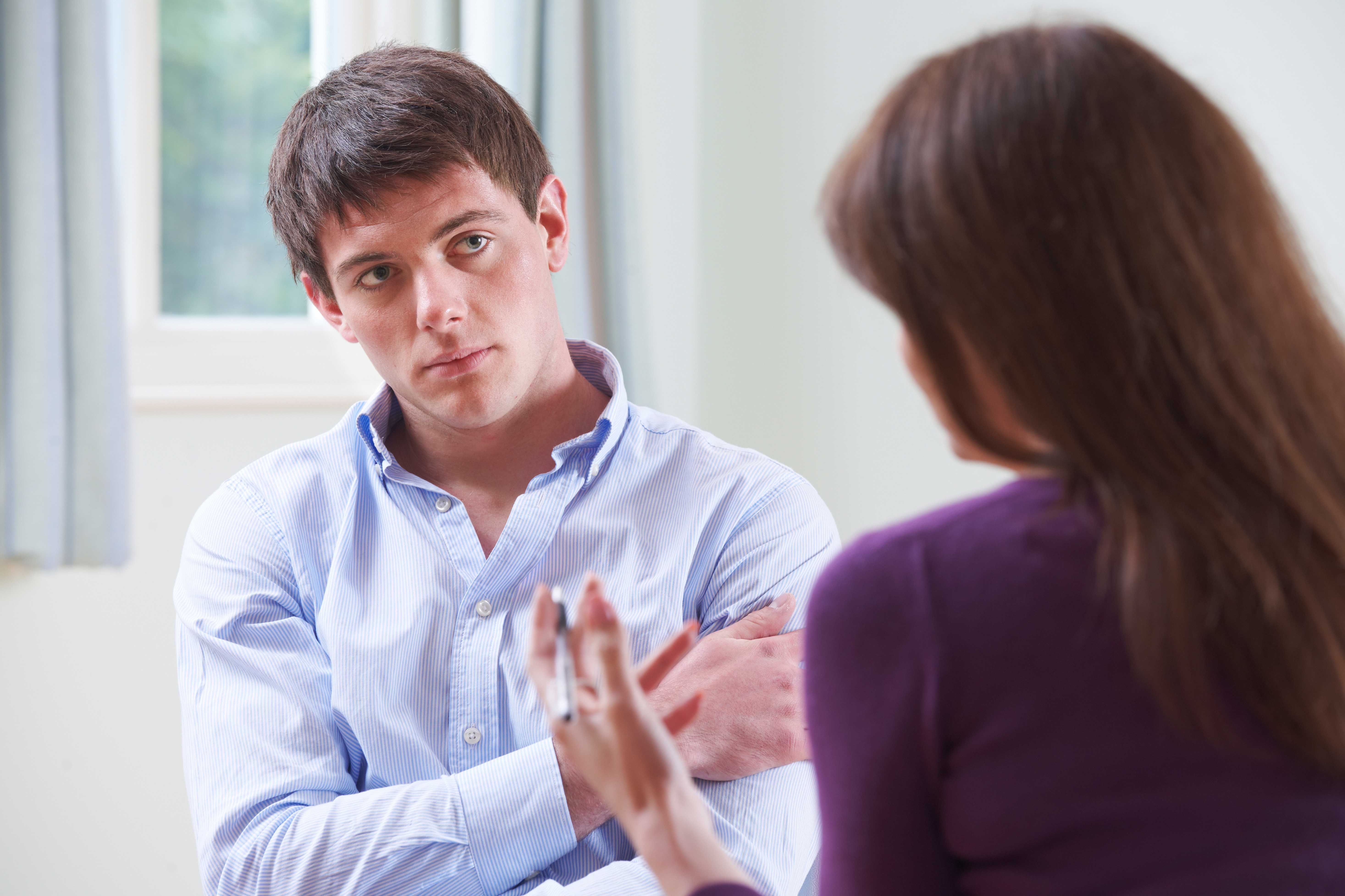 A man sat in a chair with his arm across his chest, listening intently to a woman sat with her back to the camera
